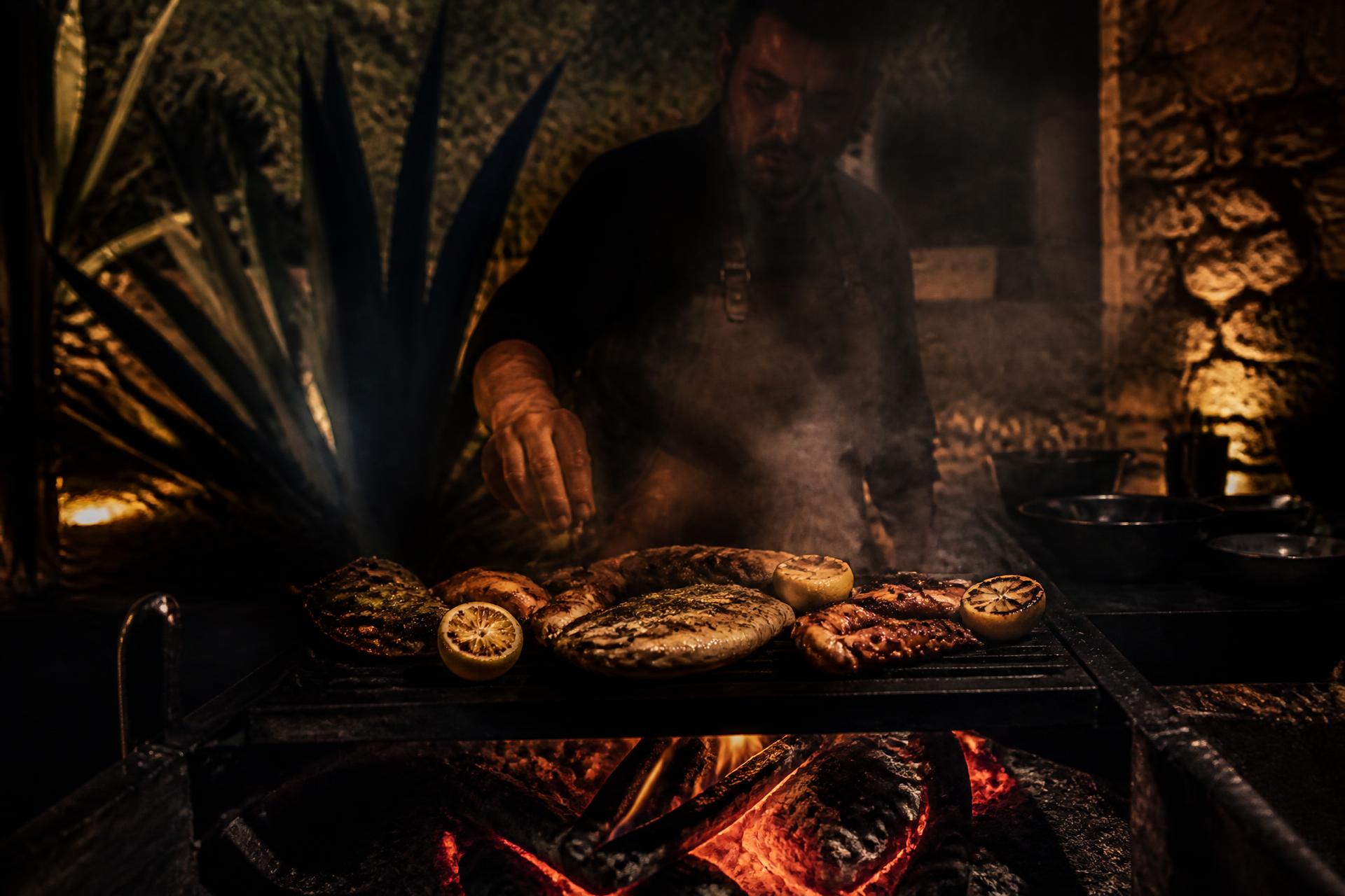 Open fire grill with seafood and charred citrus in a dark courtyard kitchen